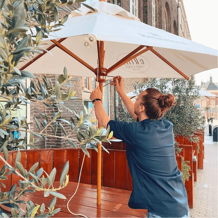 Een medewerker zet de parasol open boven het terras aan de Visstraat